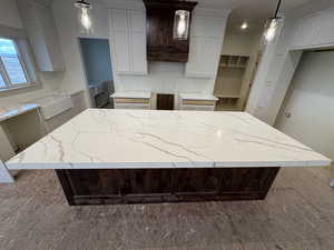 Kitchen with decorative light fixtures, light stone countertops, custom exhaust hood, and a kitchen island