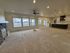 Unfurnished living room featuring ceiling fan with notable chandelier and a stone fireplace