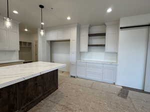 Kitchen featuring white cabinetry, pendant lighting, and light stone countertops