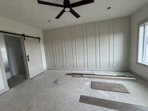 Unfurnished room with ceiling fan, a barn door, and plenty of natural light