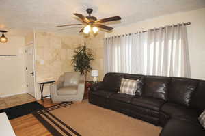 Living room with a textured ceiling, ceiling fan, tile walls, and light hardwood / wood-style flooring