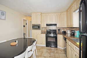 Kitchen with a textured ceiling, stainless steel appliances, dark stone countertops, and backsplash