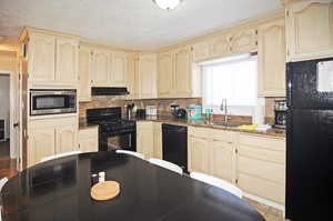 Kitchen with sink, a textured ceiling, black appliances, and tasteful backsplash