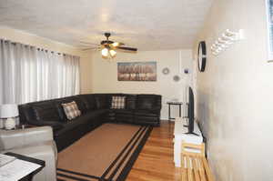 Living room with a textured ceiling, ceiling fan, and hardwood / wood-style flooring