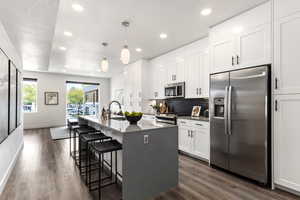 Kitchen featuring pendant lighting, a center island with sink, a kitchen bar, appliances with stainless steel finishes, and white cabinets. This is the model home.