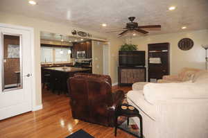 Living room featuring ceiling fan, a textured ceiling, and light wood-type flooring