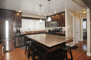 Kitchen with light stone countertops, a center island, stainless steel appliances, a kitchen breakfast bar, and sink