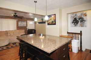 Kitchen with decorative light fixtures, hardwood / wood-style floors, a breakfast bar, dark brown cabinets, and light stone counters