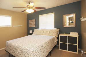 Carpeted bedroom featuring ceiling fan and a textured ceiling