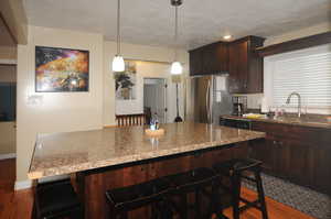 Kitchen with light stone counters, a kitchen breakfast bar, stainless steel fridge, and sink