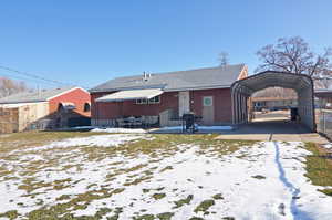 Snow covered back of property featuring a carport