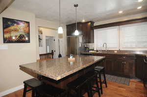 Kitchen with a kitchen bar, sink, dark wood-type flooring, and stainless steel refrigerator