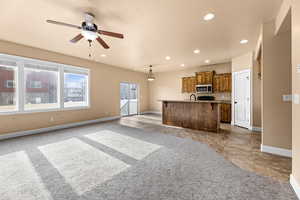 Kitchen with an island with sink, ceiling fan, decorative light fixtures, a kitchen breakfast bar, and sink