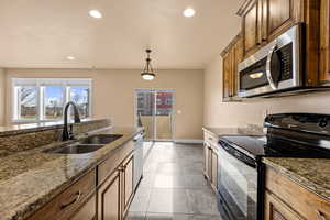 Kitchen with appliances with stainless steel finishes, sink, hanging light fixtures, light tile patterned flooring, and stone counters