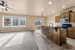 Kitchen with a breakfast bar area, ceiling fan, decorative light fixtures, a kitchen island with sink, and black electric range oven