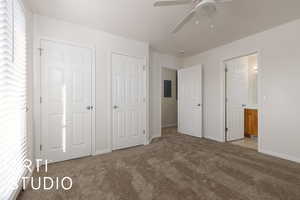 Unfurnished bedroom with ceiling fan, light colored carpet, connected bathroom, and multiple closets