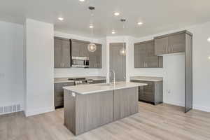 Kitchen featuring decorative light fixtures, a center island with sink, sink, light wood-type flooring, and stainless steel appliances