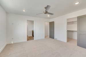 Unfurnished bedroom featuring ceiling fan, light colored carpet, ensuite bath, a spacious closet, and a closet