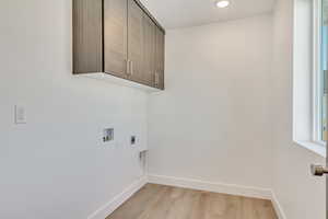 Clothes washing area with cabinets, light hardwood / wood-style floors, hookup for a washing machine, and electric dryer hookup