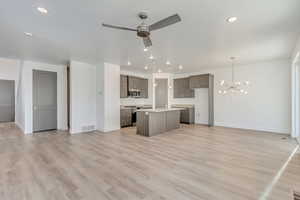 Kitchen with ceiling fan with notable chandelier, appliances with stainless steel finishes, decorative light fixtures, an island with sink, and sink