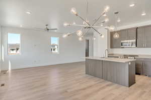 Kitchen with plenty of natural light, sink, ceiling fan with notable chandelier, and a center island with sink