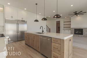 Kitchen with white cabinets, appliances with stainless steel finishes, decorative light fixtures, sink, and a center island with sink