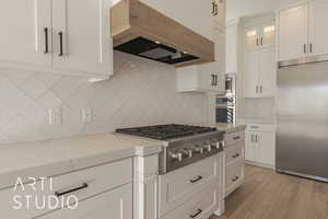 Kitchen featuring light stone countertops, white cabinets, built in appliances, decorative backsplash, and premium range hood