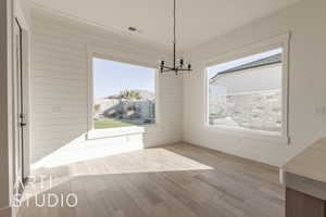 Unfurnished dining area with plenty of natural light, light wood-type flooring, and an inviting chandelier