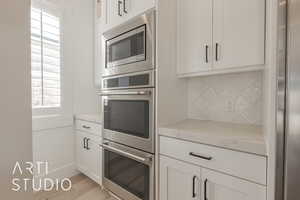 Kitchen with decorative backsplash, appliances with stainless steel finishes, a wealth of natural light, and light stone counters