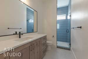 Bathroom with an enclosed shower, vanity, tile patterned flooring, and toilet