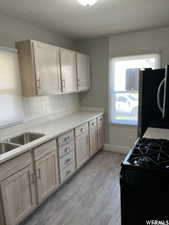 Kitchen with light wood-type flooring, black range with gas stovetop, light brown cabinets, and stainless steel refrigerator