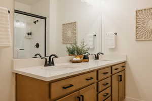 Bathroom featuring a tile shower, double vanity, and a sink