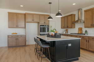 Kitchen featuring wall chimney range hood, a center island, appliances with stainless steel finishes, light countertops, and light wood finished floors