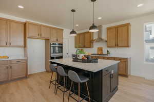 Kitchen featuring baseboards, wall chimney range hood, light wood-style flooring, light countertops, and a kitchen island
