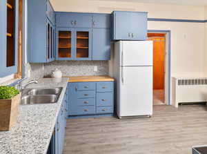 Kitchen with sink, radiator, blue cabinetry, and white fridge