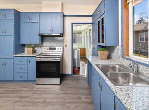 Kitchen featuring sink, blue cabinets, backsplash, and electric stove