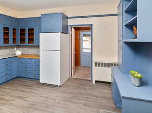 Kitchen with radiator, white fridge, backsplash, light hardwood / wood-style flooring, and blue cabinets