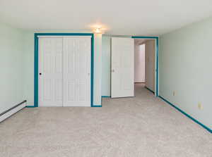 Unfurnished bedroom with baseboard heating, light colored carpet, and a closet