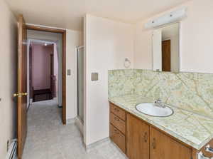 Bathroom featuring a shower with shower door, a baseboard radiator, backsplash, and vanity