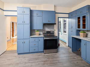 Kitchen featuring light hardwood / wood-style floors, blue cabinetry, decorative backsplash, and stainless steel range with electric stovetop