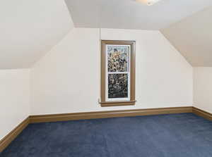 Bonus room with dark colored carpet and vaulted ceiling