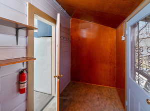 Interior space with a healthy amount of sunlight, vaulted ceiling, and wood walls