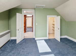 Additional living space featuring lofted ceiling, radiator heating unit, and dark carpet