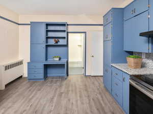 Kitchen featuring blue cabinetry, electric stove, light wood-type flooring, light stone countertops, and radiator heating unit