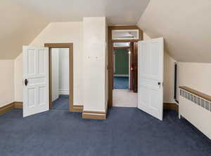 Additional living space featuring radiator heating unit, lofted ceiling, and dark colored carpet