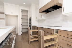 Kitchen featuring appliances with stainless steel finishes, white cabinetry, decorative backsplash, premium range hood, and dark hardwood / wood-style floors