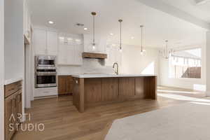 Kitchen featuring backsplash, a spacious island, white cabinetry, light hardwood / wood-style flooring, and stainless steel appliances