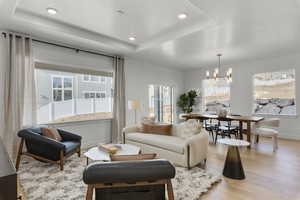 Living room featuring light wood-type flooring, a notable chandelier, and a tray ceiling