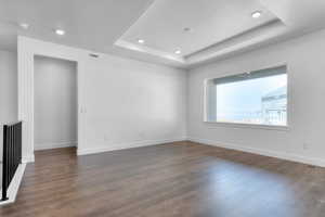 Spare room with baseboards, dark wood-style flooring, a tray ceiling, and recessed lighting