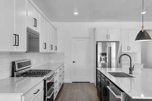 Kitchen with a sink, decorative light fixtures, appliances with stainless steel finishes, light stone countertops, and dark wood-type flooring